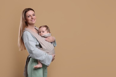 Mother holding her child in sling (baby carrier) on light brown background. Space for text