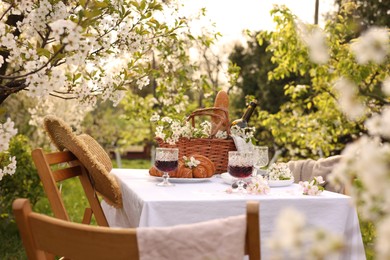 Photo of Stylish table setting with beautiful spring flowers, wine and croissants in garden