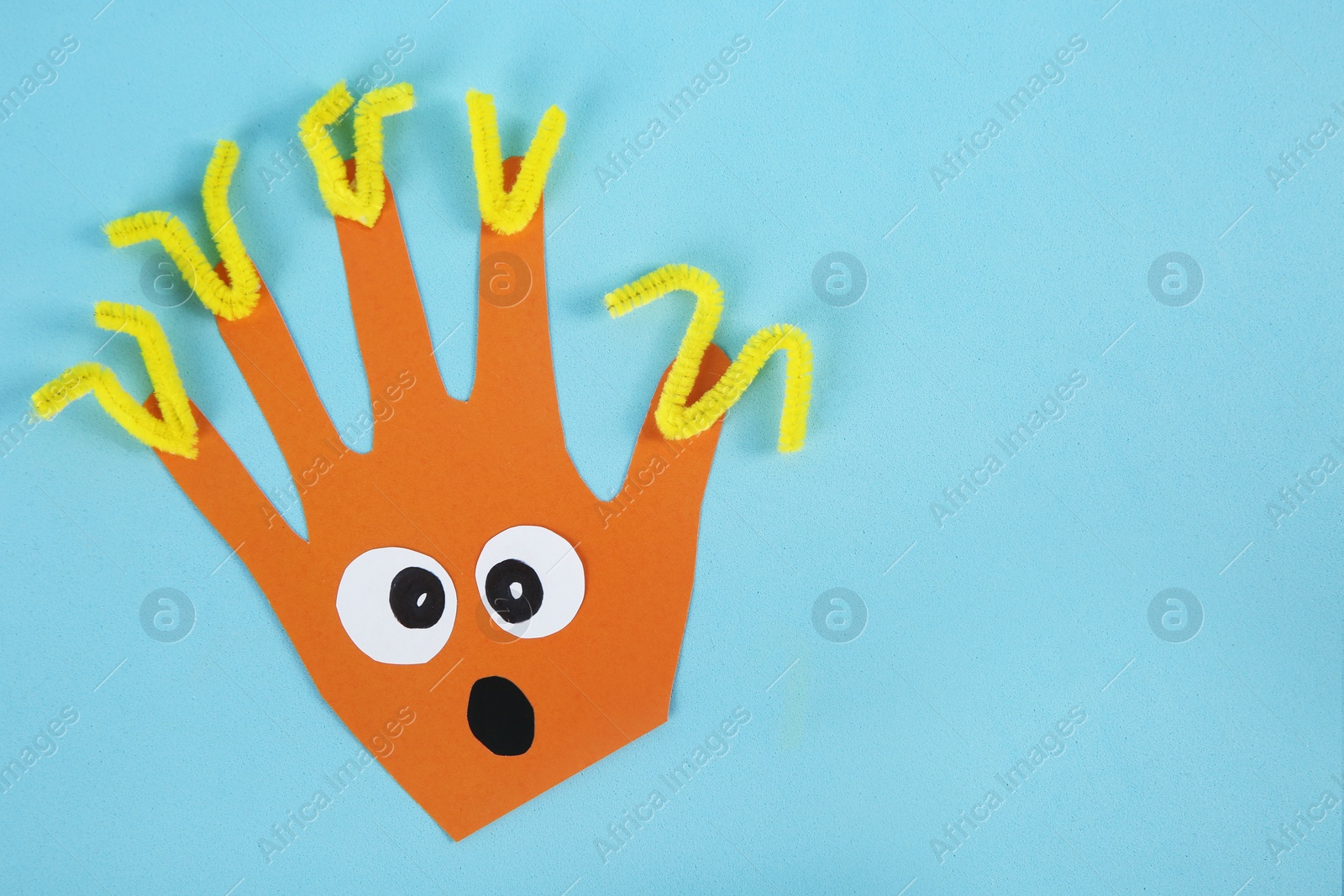 Photo of Funny orange hand shaped monster on light blue background, top view with space for text. Halloween decoration