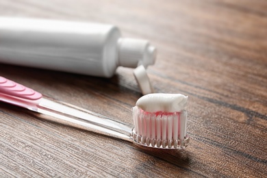 Photo of Toothbrush and tube of paste on wooden table, closeup