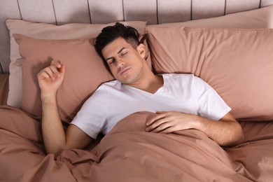 Man sleeping in comfortable bed with beige linens