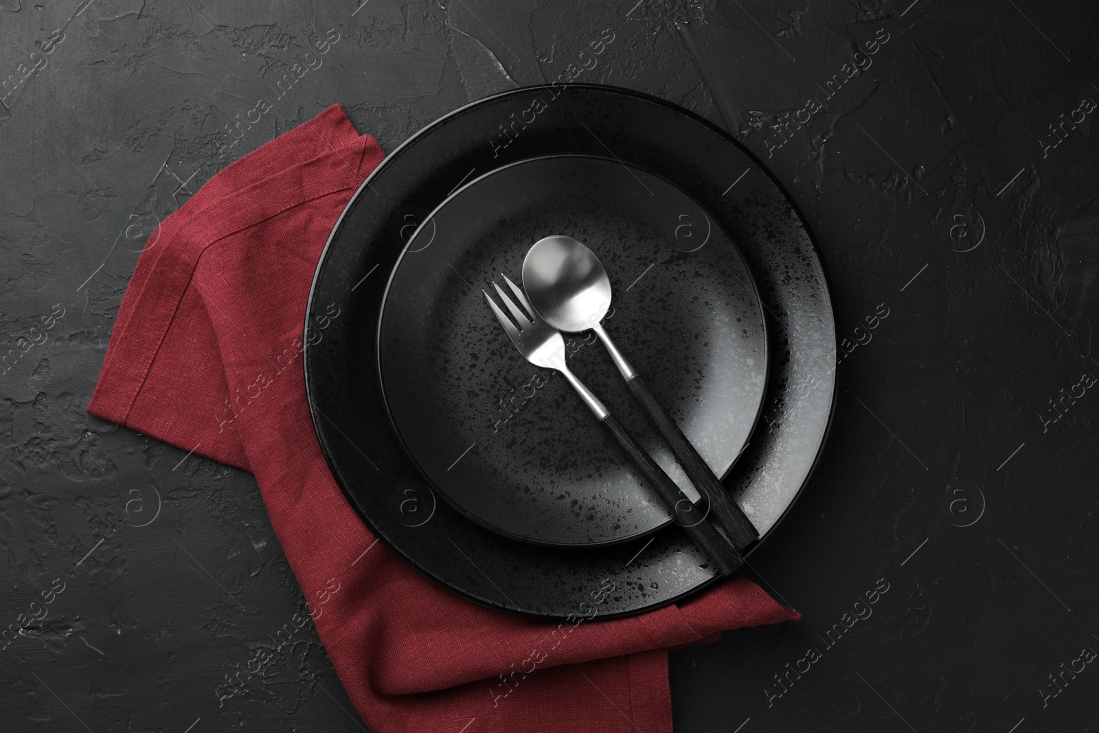 Photo of Stylish setting with cutlery, napkin and plates on dark textured table, top view