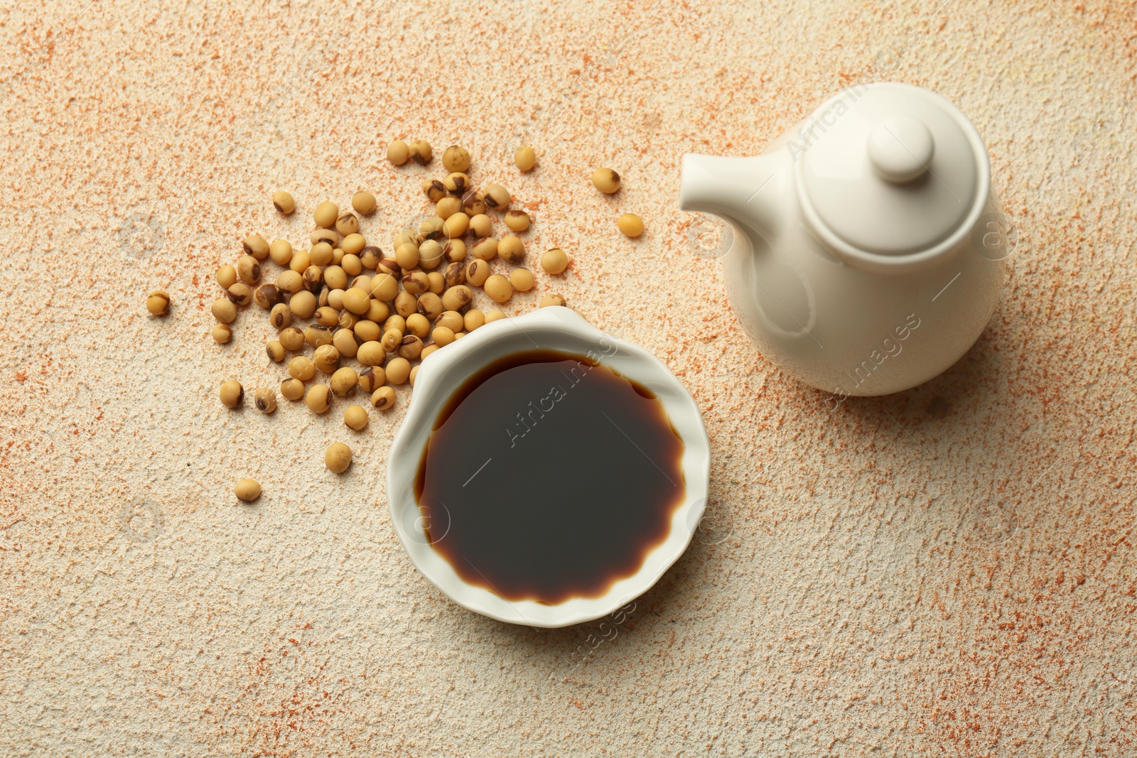 Photo of Soy sauce in bowl and beans on beige textured table, flat lay