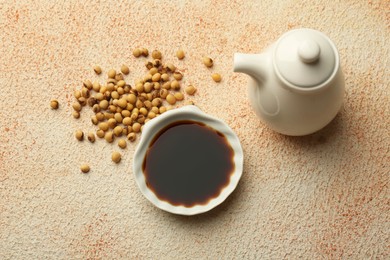 Photo of Soy sauce in bowl and beans on beige textured table, flat lay