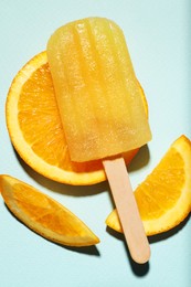 Photo of Tasty orange ice pop on pale light blue background, top view. Fruit popsicle