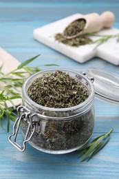 Jar of dry tarragon and green leaves on light blue wooden table