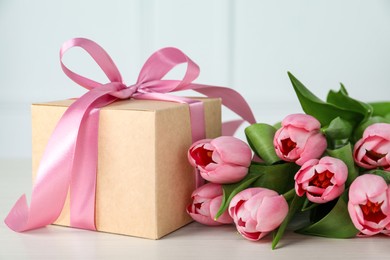 Photo of Beautiful gift box with bow and pink tulip flowers on white table, closeup