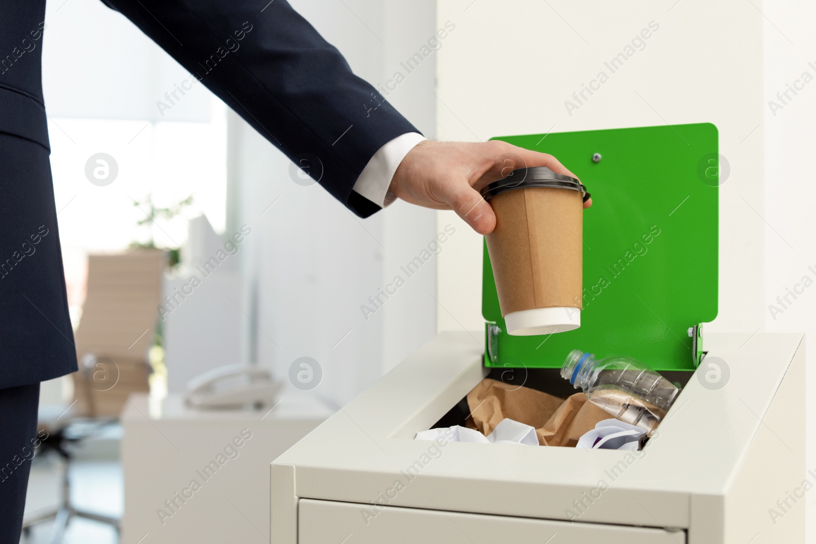 Photo of Man putting used paper cup into trash bin in office, closeup. Waste recycling