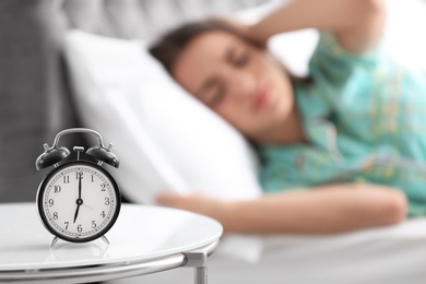 Alarm clock on table and woman in bedroom. Sleeping time