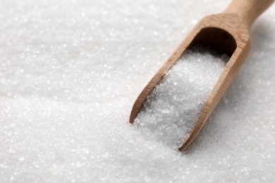 Photo of Wooden scoop on granulated sugar, closeup. Space for text