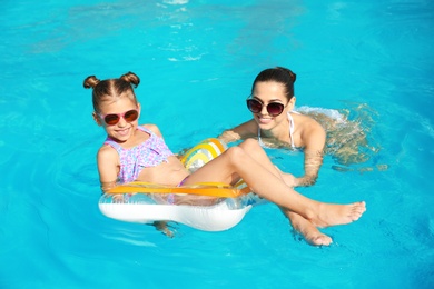 Young mother with little daughter in swimming pool on sunny day
