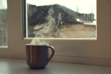 Cup of hot drink near window on rainy day. Space for text