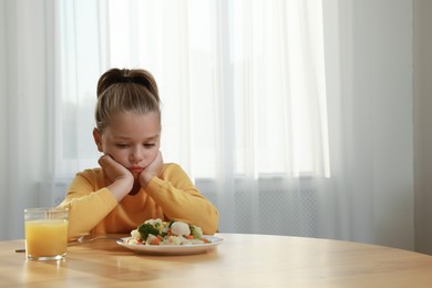 Photo of Cute little girl refusing to eat vegetable salad at home, space for text
