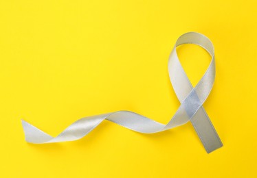 International Psoriasis Day. Ribbon as symbol of support on yellow background, top view. Space for text