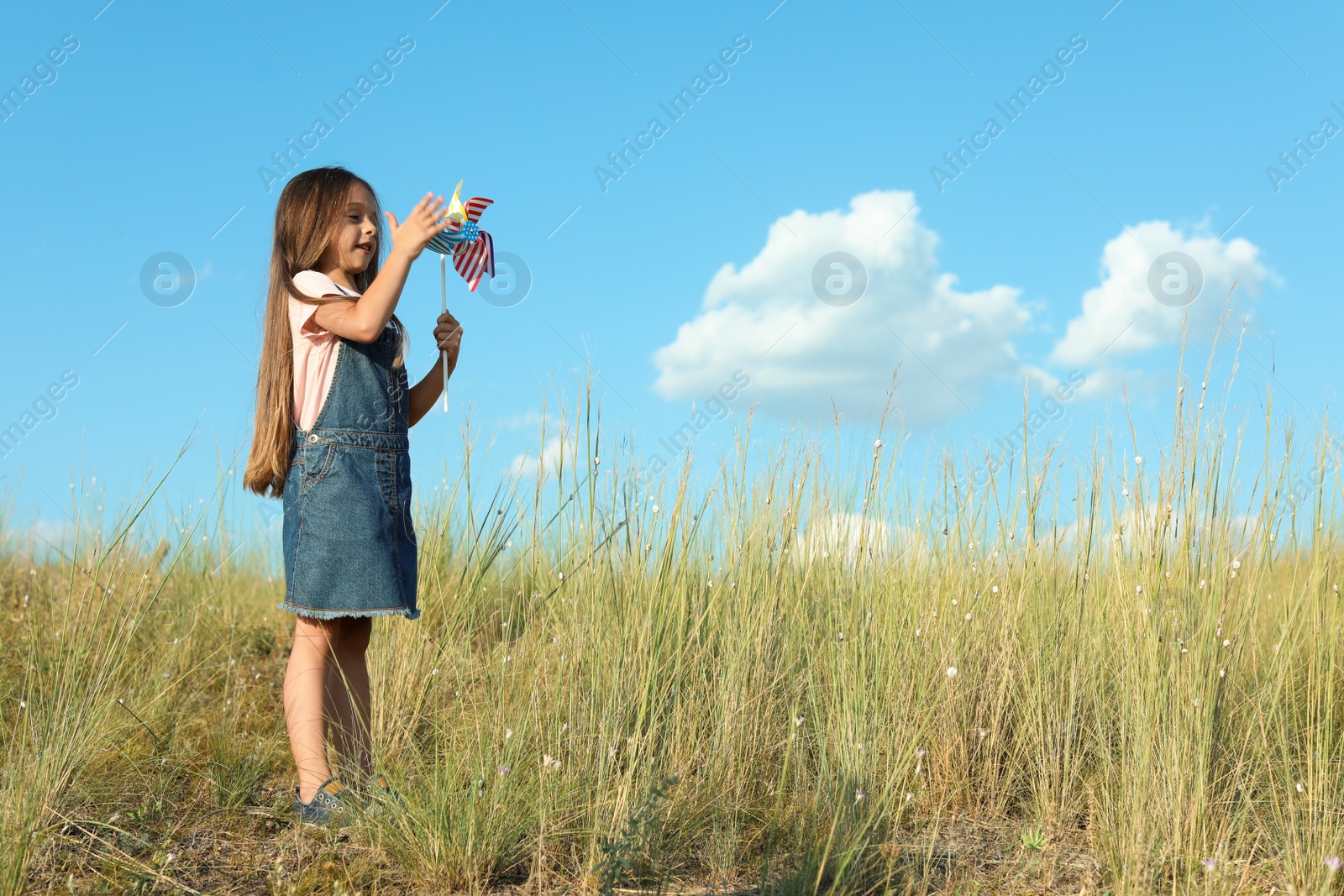 Photo of Cute little girl with pinwheel outdoors, space for text. Child spending time in nature