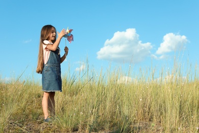 Photo of Cute little girl with pinwheel outdoors, space for text. Child spending time in nature
