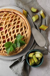 Photo of Freshly baked rhubarb pie, cut stalks and cake server on light grey table, flat lay