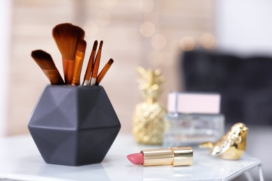 Photo of Makeup brushes in holder and lipstick on table indoors