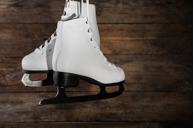 Photo of Pair of white ice skates hanging on wooden background. Space for text