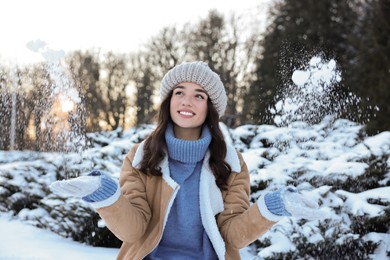 Portrait of smiling woman playing with snow in winter park