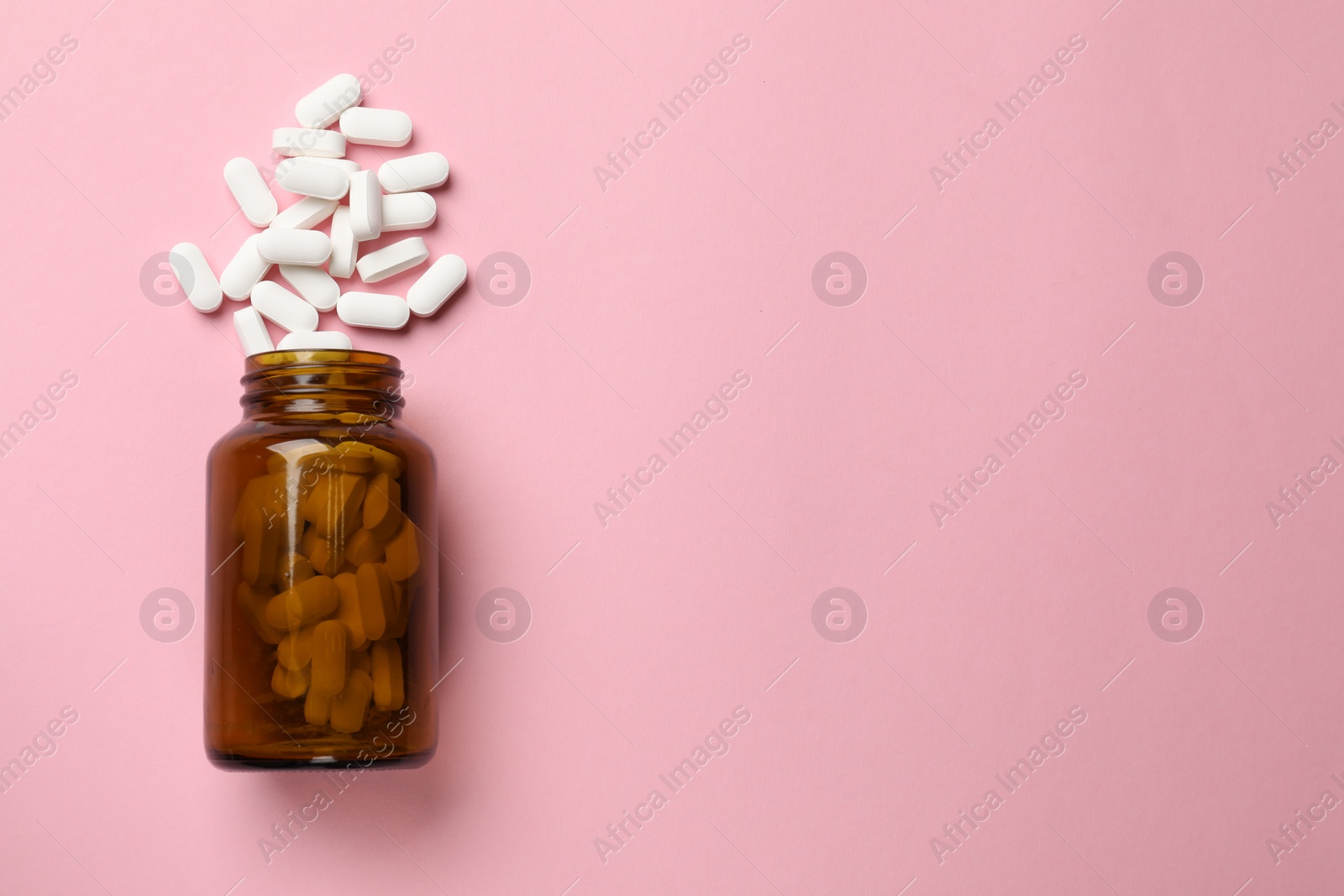 Photo of Bottle and vitamin capsules on pink background, top view. Space for text