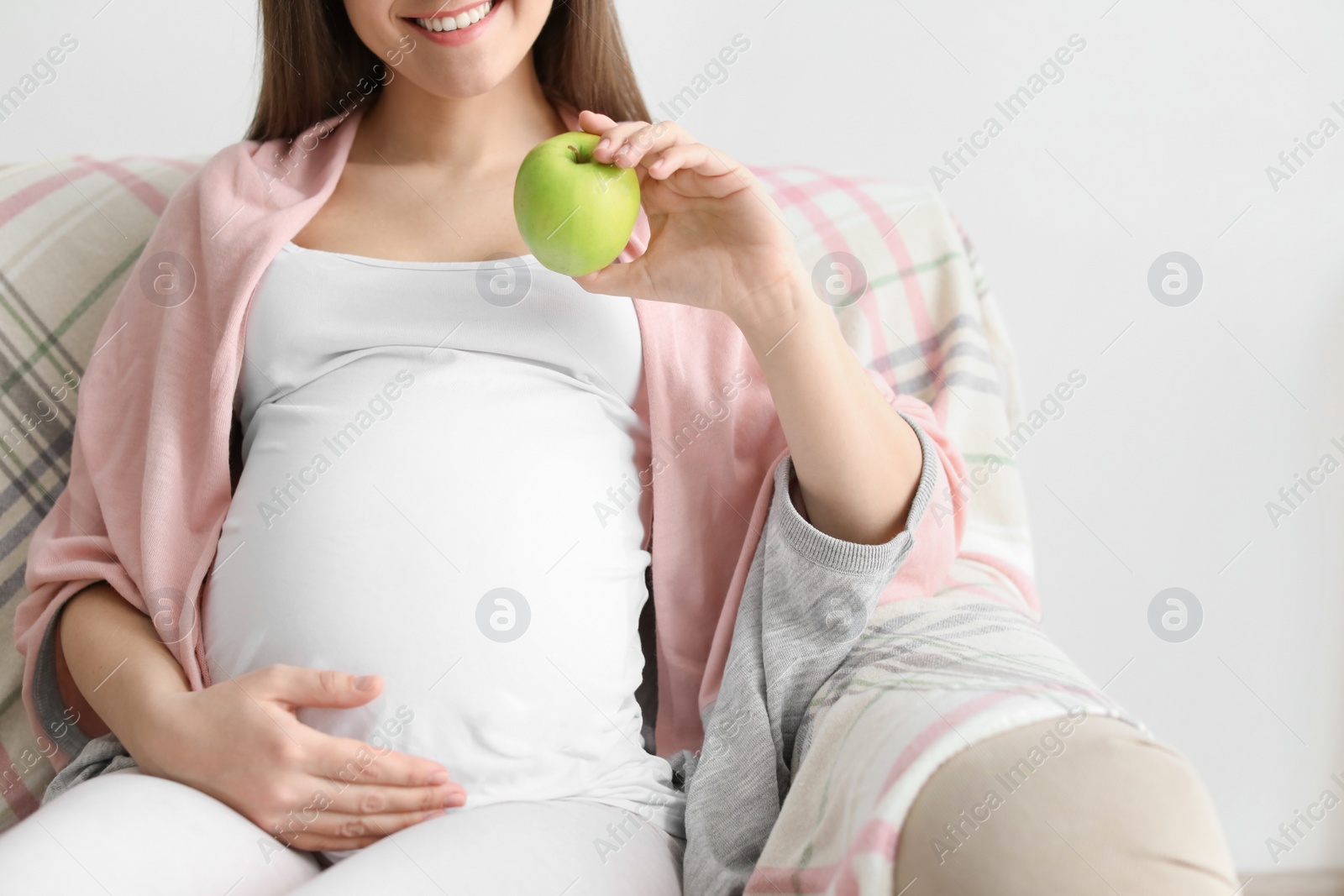 Photo of Young pregnant woman holding apple at home