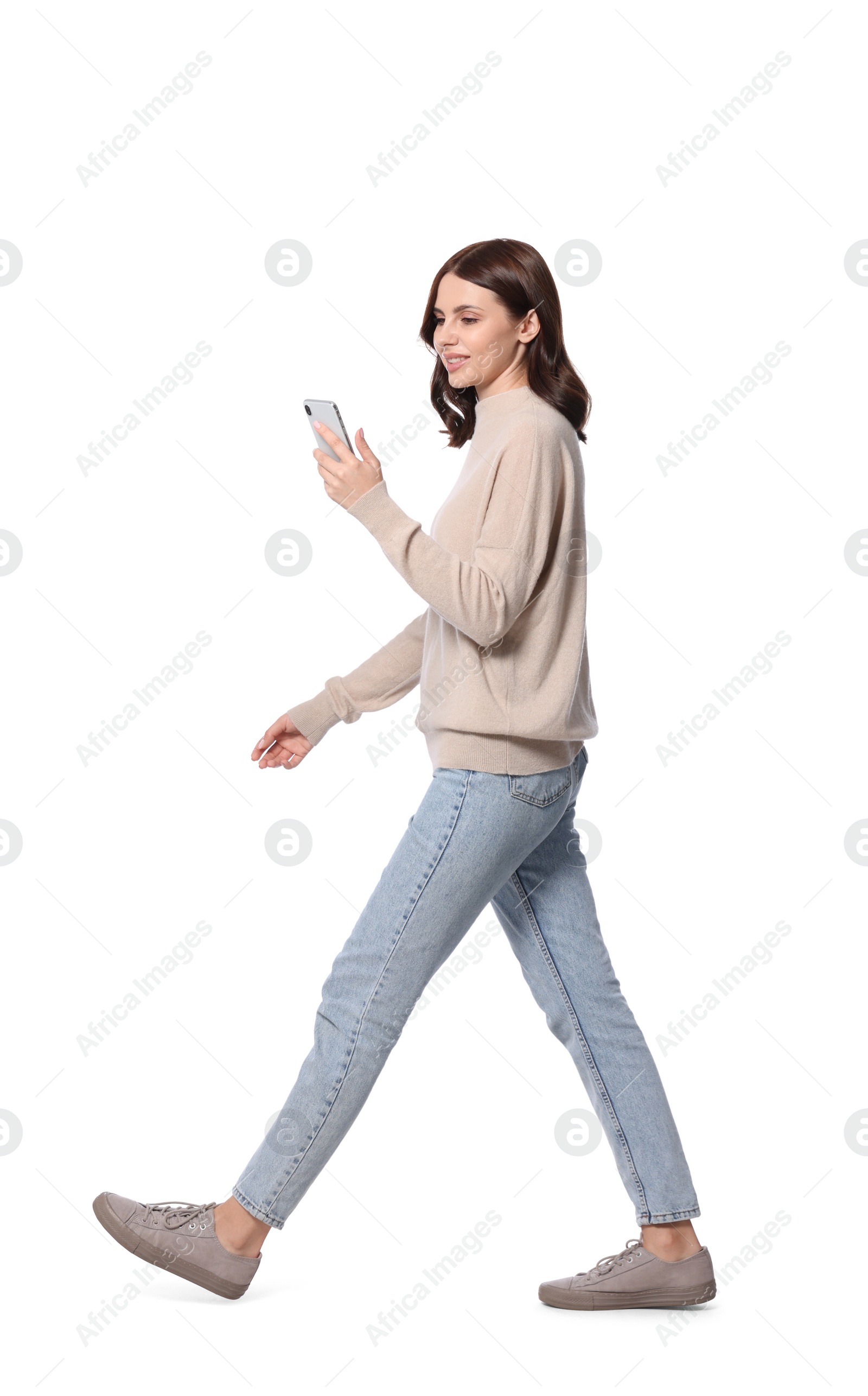 Photo of Beautiful young woman in casual outfit using smartphone while walking on white background