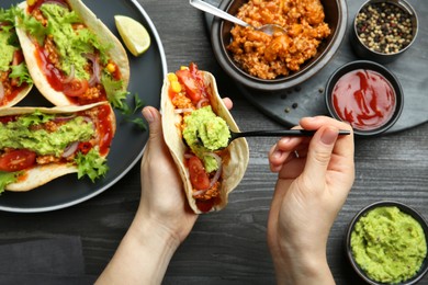 Photo of Woman adding guacamole to delicious taco at wooden table, top view