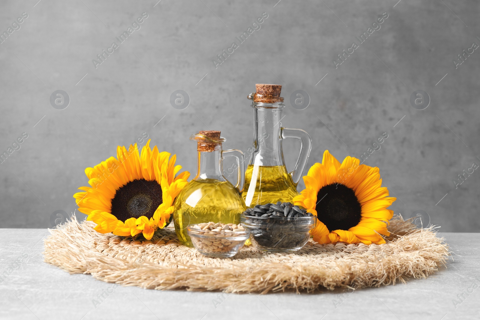 Photo of Sunflower cooking oil, seeds and yellow flowers on light grey table