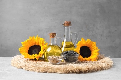 Sunflower cooking oil, seeds and yellow flowers on light grey table