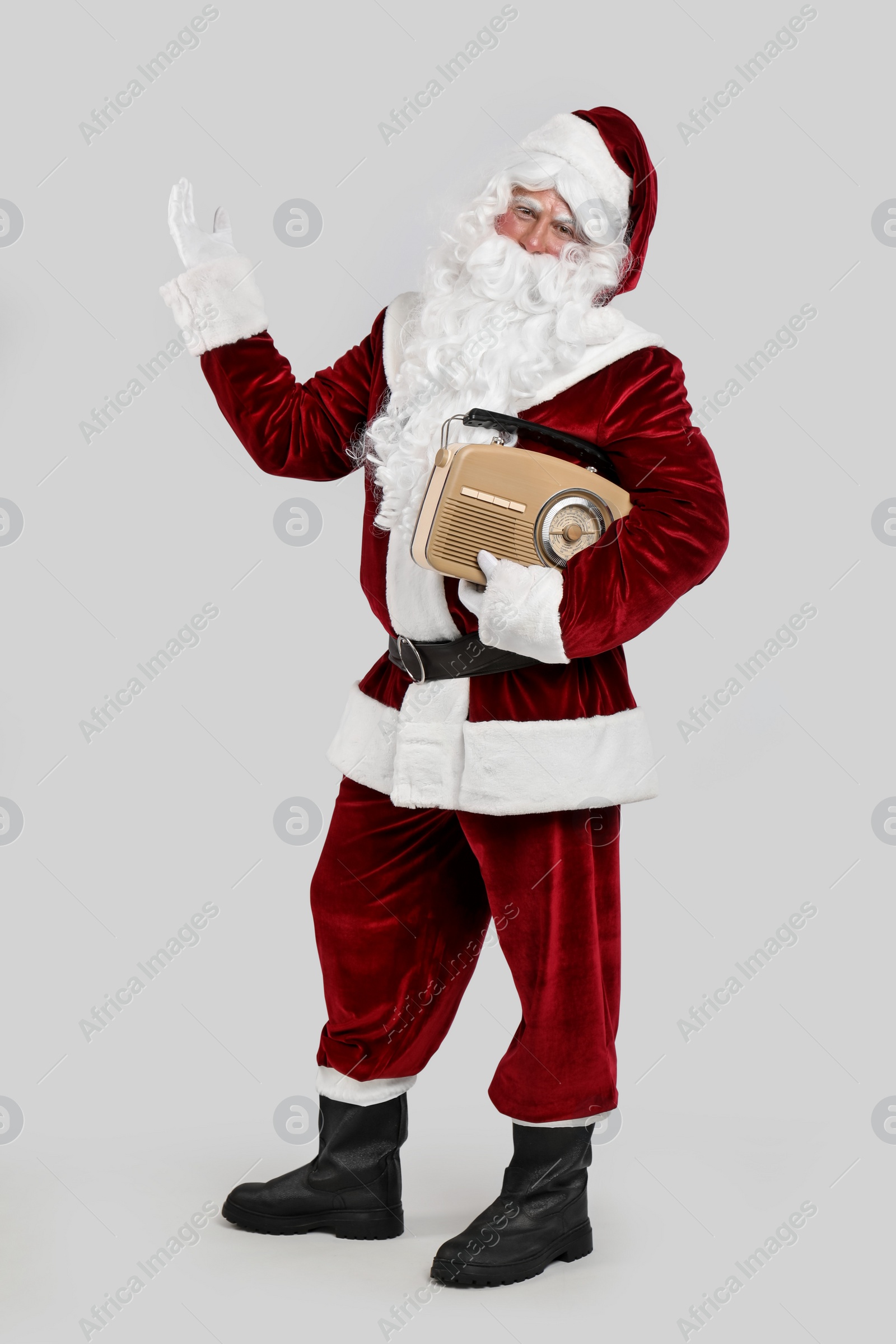 Photo of Santa Claus with vintage radio on light grey background. Christmas music