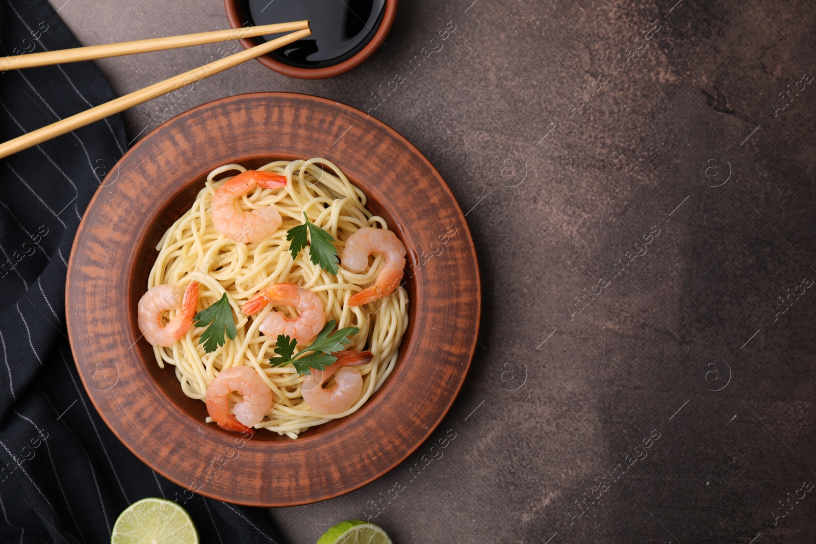 Photo of Tasty spaghetti with shrimps, and parsley on brown textured table, flat lay. Space for text