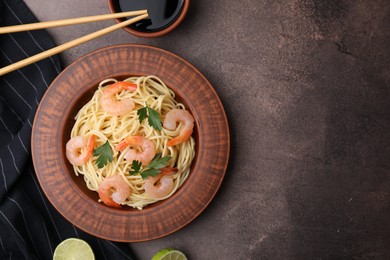 Photo of Tasty spaghetti with shrimps, and parsley on brown textured table, flat lay. Space for text