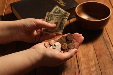 Donate and give concept. Woman holding coins and dollar banknote at wooden table, closeup