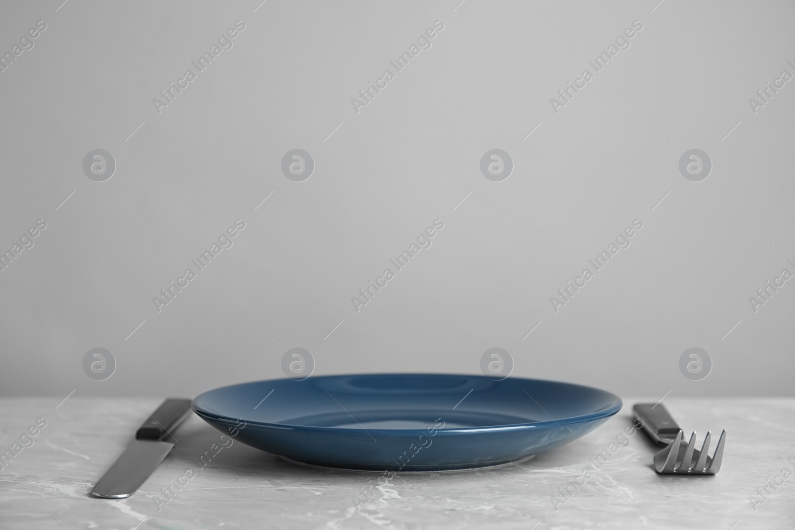 Photo of Empty blue ceramic plate with cutlery on light grey marble table