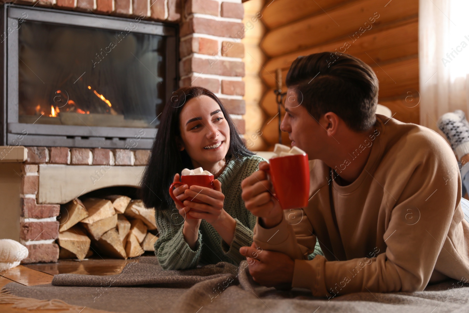 Photo of Lovely couple with sweet cocoa near fireplace indoors