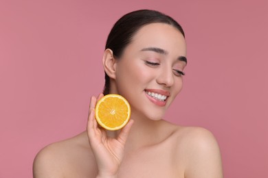 Beautiful young woman with piece of orange on pink background