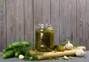 Photo of Glass jar of pickled cucumbers and ingredients on grey wooden table