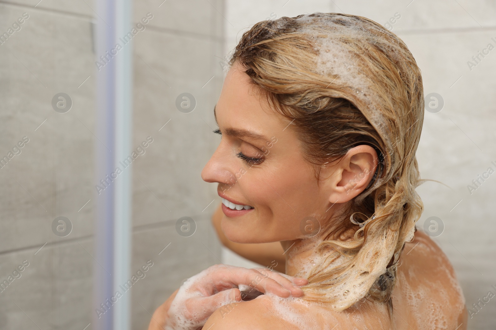 Photo of Beautiful happy woman washing hair in shower. Space for text