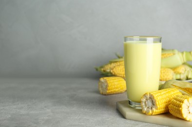Photo of Tasty fresh corn milk in glass and cobs on light grey table. Space for text