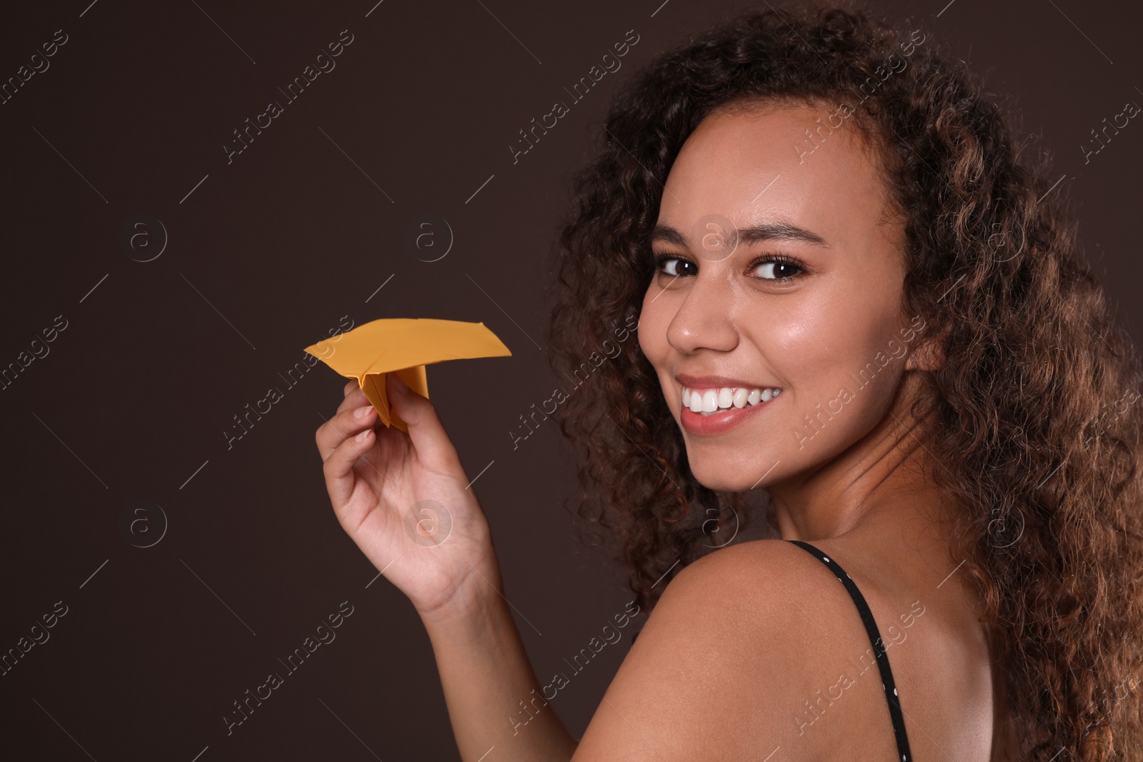 Photo of Beautiful African-American woman playing with paper plane on brown background