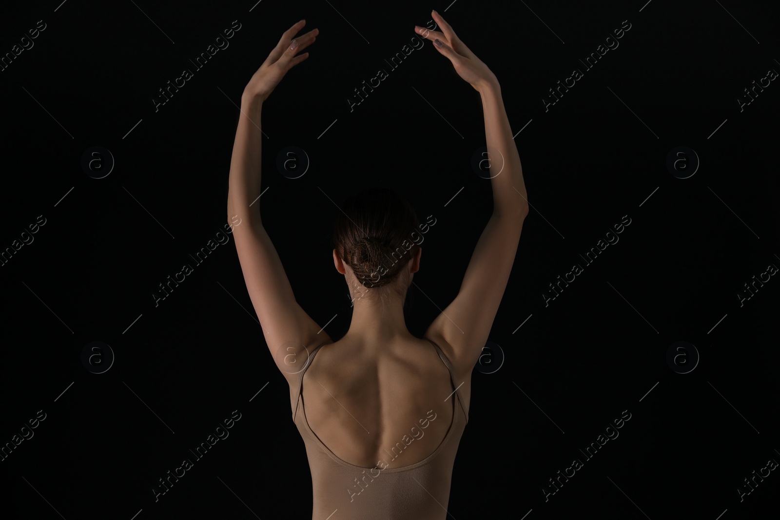 Photo of Young ballerina dancing on black background, back view