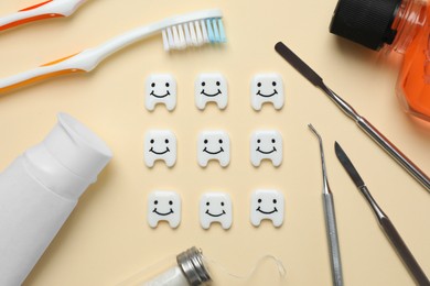 Photo of Plastic teeth with cute faces, oral care products and dental tools on beige background, flat lay