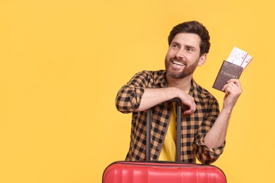 Smiling man with passport, tickets and suitcase on yellow background. Space for text