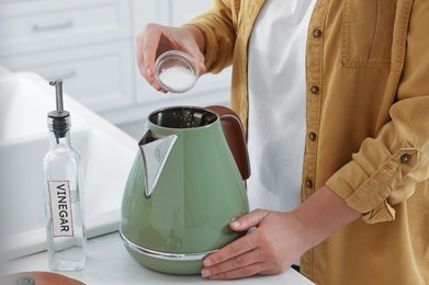 Photo of Woman adding baking soda into electric kettle in kitchen, closeup