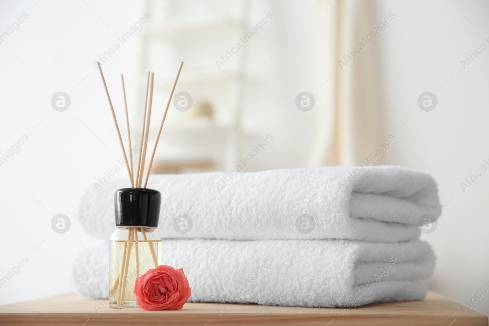 Photo of Reed air freshener and stack of towels on table against blurred background