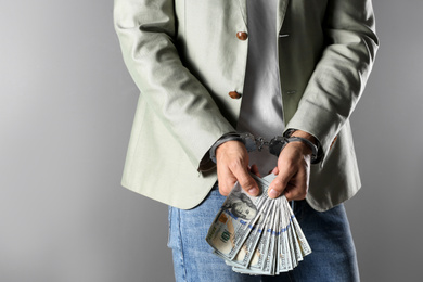 Photo of Man in handcuffs holding bribe money on grey background, closeup