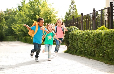 Cute little children with backpacks running outdoors. Elementary school