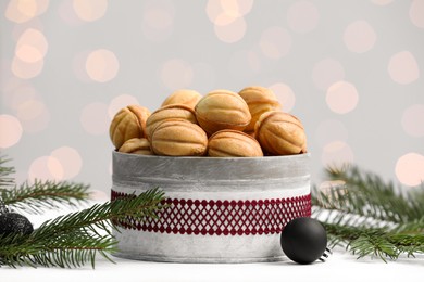 Homemade walnut shaped cookies with boiled condensed milk near fir branches and balls on white table. Bokeh effect