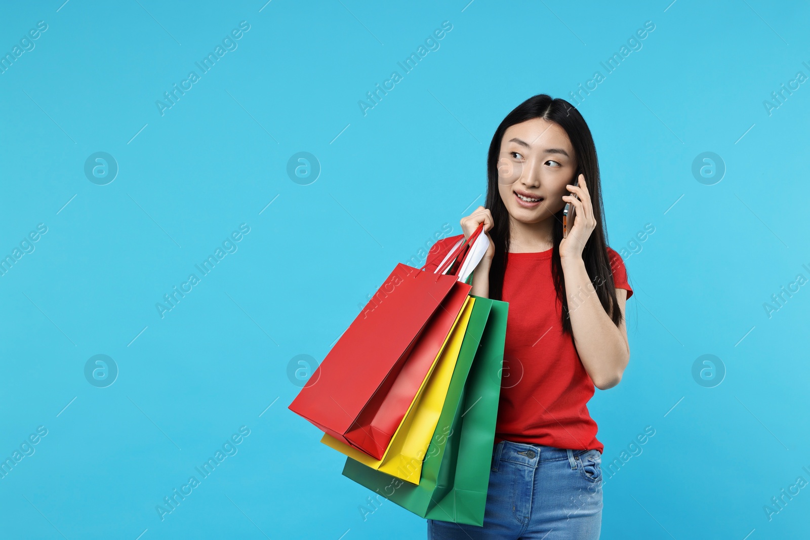 Photo of Smiling woman with shopping bags talking by smartphone on light blue background. Space for text